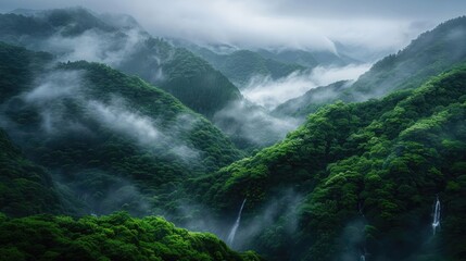 A breathtaking view of misty green mountains and cascading waterfalls enveloped in fog. Captivating nature and serene landscape photography.