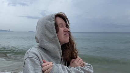 Young woman shivering and trembling from cold rainy weather at summer vacation on beach, sea