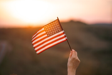 Woman`s hand holding a waving american USA flag in magic sunset.