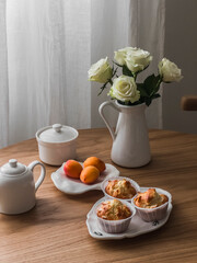 Almond mini cakes, tea utensils, white roses in a ceramic vase on a round wooden table in the...