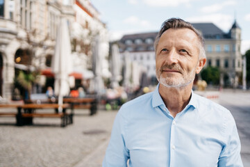 A mature man with gray hair and beard enjoying a sunny day outdoors in an urban setting, exuding confidence and contentment.