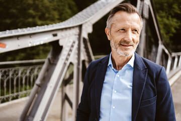 Confident mature man in a blue suit posing outdoors on a steel bridge. Represents success,...