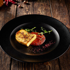 Pan-fried cheese with berry sauce, served on a black plate with a rustic wooden background