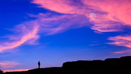 silhouette small tourist stand alone on the mountain rock  looking blue and pink sky