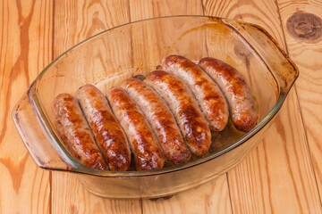 Baked pork sausages on glass casserole pan on rustic table
