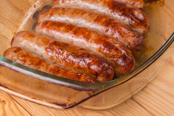 Baked pork sausages on glass casserole pan, fragment close-up
