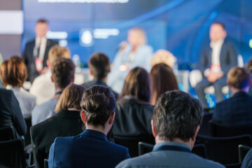 Focused audience listening to speakers at a business conference panel discussion. Event promotes networking and professional development opportunities.