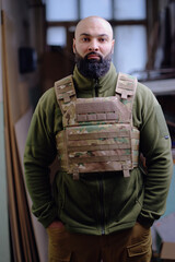 Bald bearded military man wearing buletproof vest looking in camera