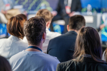 Audience members attentively listening to a speaker at a business conference. People are focused...