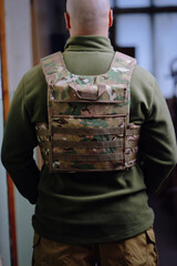Bald bearded military man wearing buletproof vest from back