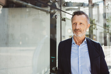 Fototapeta premium Confident mature businessman standing outdoors near a modern glass building, exuding professionalism and leadership. Perfect for business, leadership, or corporate-themed visuals.