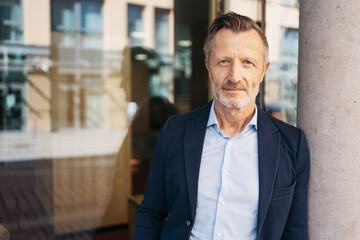 Fototapeta premium Portrait of a confident mature businessman standing against a pillar in an urban setting, conveying professionalism and experience.