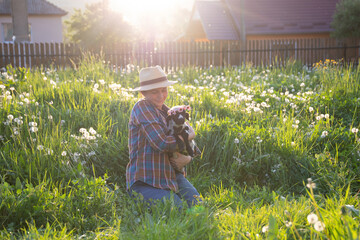 Cheerful woman with a hat sitting in green grass, holding a cute little lamb