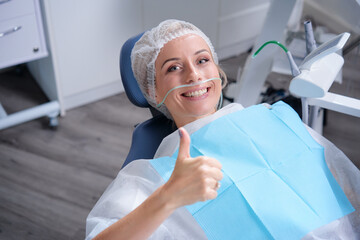 Young smiling woman showing thumb up in dentist chair