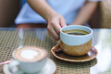 Closeup image of a woman holding and drinking coffee with friend in cafe
