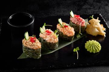 Spicy sushi assortment gunkan style with salmon, shrimp, tuna, and eel on a black slate