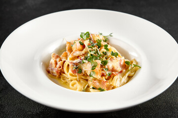 Classic carbonara pasta with a creamy sauce and garnished with fresh herbs, presented on a white plate