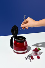 A hand places a sprig of lavender into a teapot with raspberry tea, infusing the beverage with...