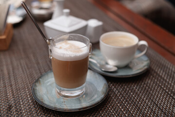 Two cups of cappuccino with latte art on wooden background. Beautiful foam, greenery ceramic cups, stylish toning