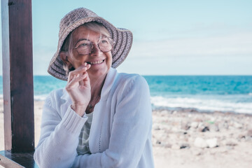 Portrait of attractive smiling senior retired woman outdoors at the sea beach wearing eyeglasses...