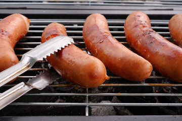 Close-up of flipping grilled sausages with metal tongues. 