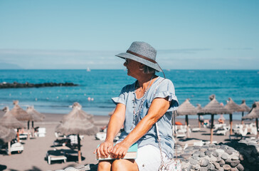 Portrait of senior woman in straw hat sitting close to the beach with a book on his legs enjoying freedom and beautiful day, relaxed senior lady in summer vacation or retirement
