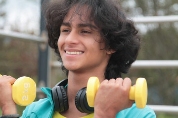 young man with headphones doing exercises with dumbbells outdoors