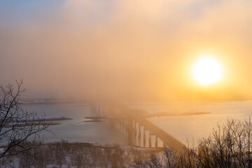 Winter view of bridge dissappearing into the fog with a low sun shining on