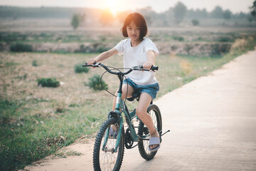 Fototapeta premium Happy little girl riding a bicycle on the road in the 
