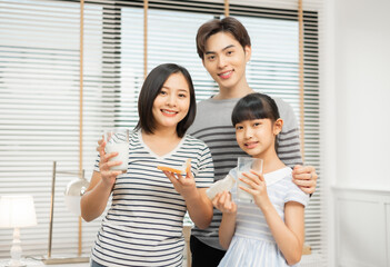 Fototapeta premium Parents and daughter enjoying breakfast with milk in a warm, inviting kitchen.Asian family breakfast scene, parents and daughter eating and drinking milk at home
