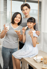 Parents and daughter enjoying breakfast with milk in a warm, inviting kitchen.Asian family breakfast scene, parents and daughter eating and drinking milk at home