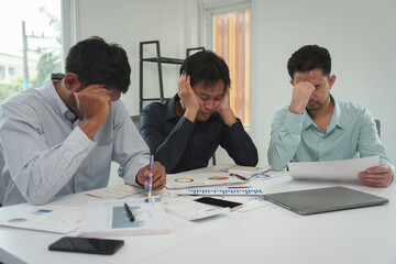 A team of tired, stressed young businessmen hold their heads in their hands. From working with...
