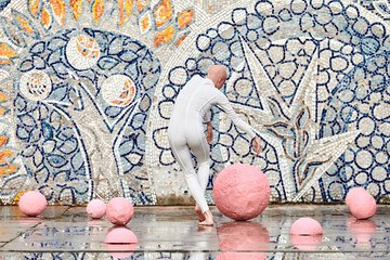 Young hairless girl ballerina with alopecia in white futuristic suit dancing outdoor among pink spheres on abstract mosaic Soviet background, symbolizes self expression and acceptance of unique beauty
