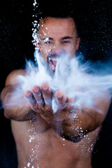 Strong shirtless man patting flour into his hands creating explosion