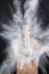 Strong shirtless man patting flour into his hands creating explosion