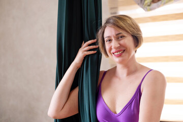 portrait of a beautiful woman, in a purple yoga suit, standing next to a green hammock, for aero...