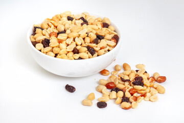 Peanut and raisin mix in round white bowl, isolated on white with loose bits around the bowl, with copy space