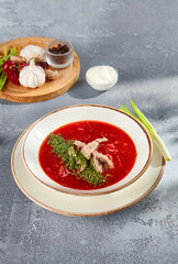 Classic beetroot borscht with beef and a dollop of sour cream, presented in a speckled bowl on a grey textured backdrop