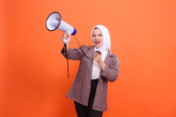 Angry young indonesia woman in hijab facing right to camera screaming candidly using mic holding...