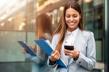 Smiling business woman using smartphone for texting, cellphone apps for work outside.