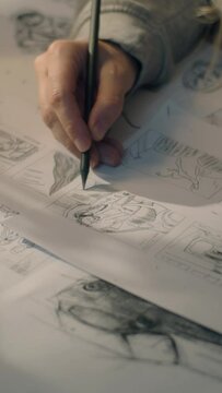 Closeup hands of a woman making pencil sketches. Working on a storyboard in a home based design studio. Woman drawing sketches as a roadmap for the video. Story telling. Vertical shot.