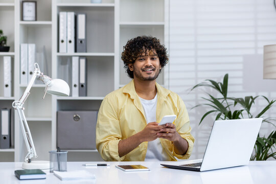 Smiling man working at home office desk with phone and laptop