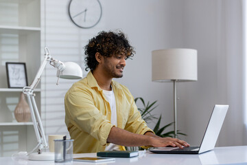 Smiling young man working on a laptop at home office desk