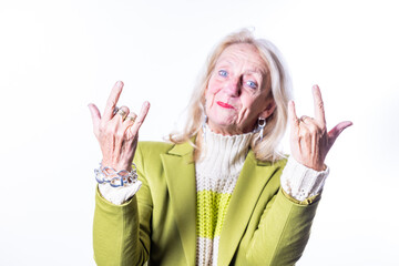 A cheerful elderly woman in a green jacket, looking joyful and relaxed, is making rock and roll hand signs