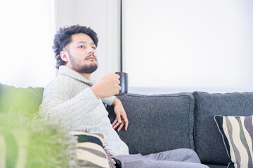 Fototapeta premium ソファーに座り、暖かい飲み物を飲む男性