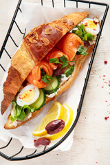 Salted healthy breakfast on light background. Fresh salmon croissant with cream cheese, cucumber, egg and salad