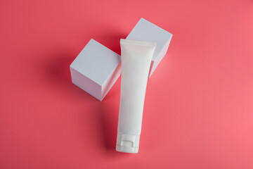 Plastic white tube for cream or lotion. Skin care or sunscreen cosmetic with stylish props on pink background.