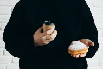 A paper cup of coffee and a heart-shaped donut in male hands, close-up.