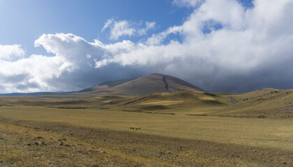 Autumn fields are partially plowed near mountains covered with dense clouds