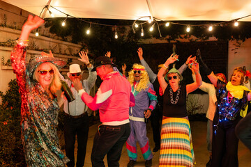 Friends in festive costumes dance and celebrate at an energetic outdoor party illuminated by string...